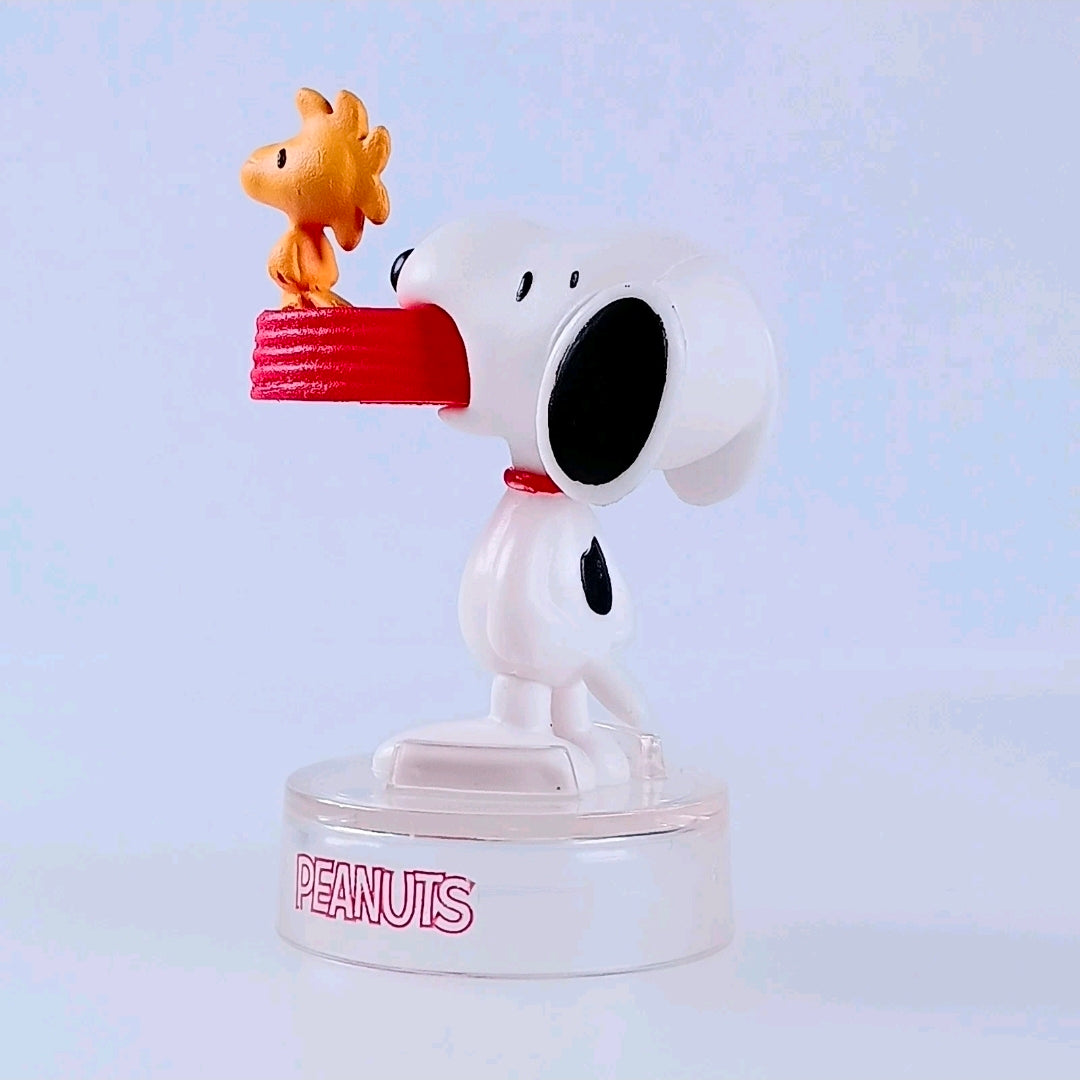 Snoopy figure holding orange bird on raised hand, clear PEANUTS base