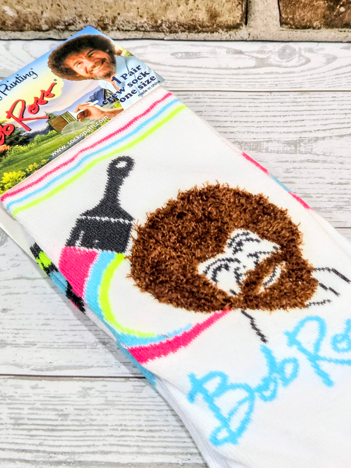 Colorful crew sock with white base, rainbow stripes, and smiling brown face graphic