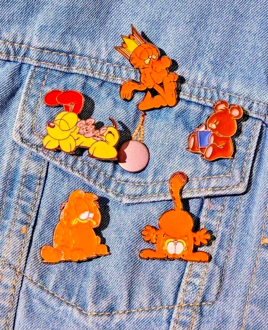 Five enamel Garfield character pins on a denim jacket, gold-outlined set