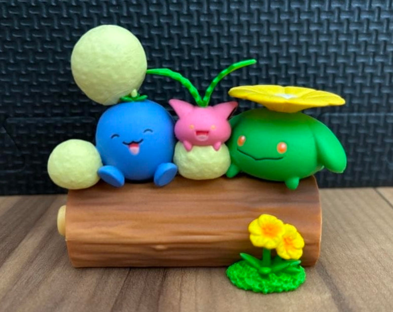 Blue, pink, and green flower-themed toy figures lying on a brown log with yellow bloom.