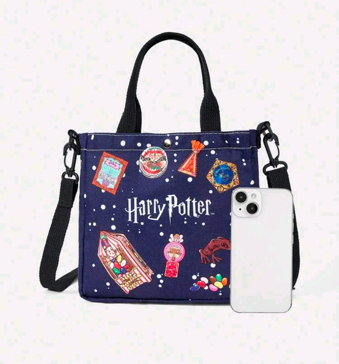 Navy canvas tote bag with printed charms, black handles, and white phone tucked on front