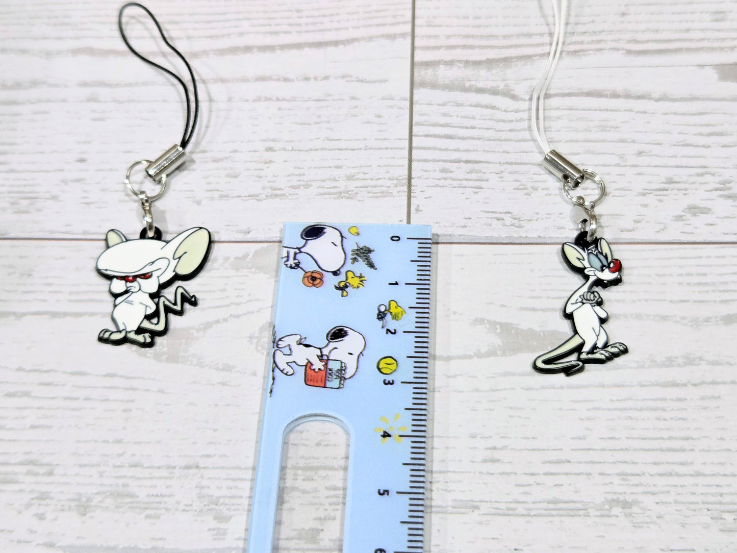 Two cartoon mouse phone keychain charms with silver clips and cords beside a ruler
