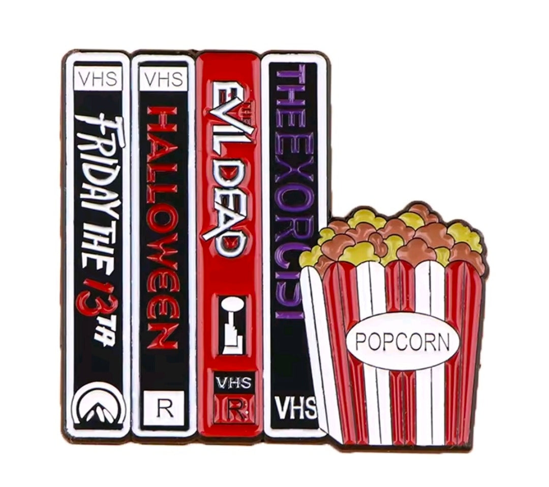 Enamel pin showing multiple VHS tapes with popcorn graphic, red and white striped design.