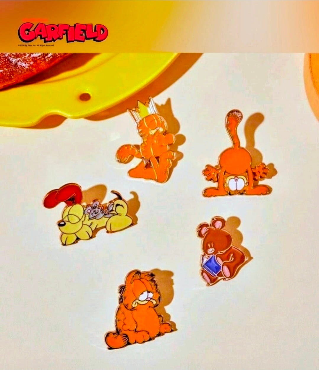 Five gold-outlined Garfield enamel pins shown on a light background