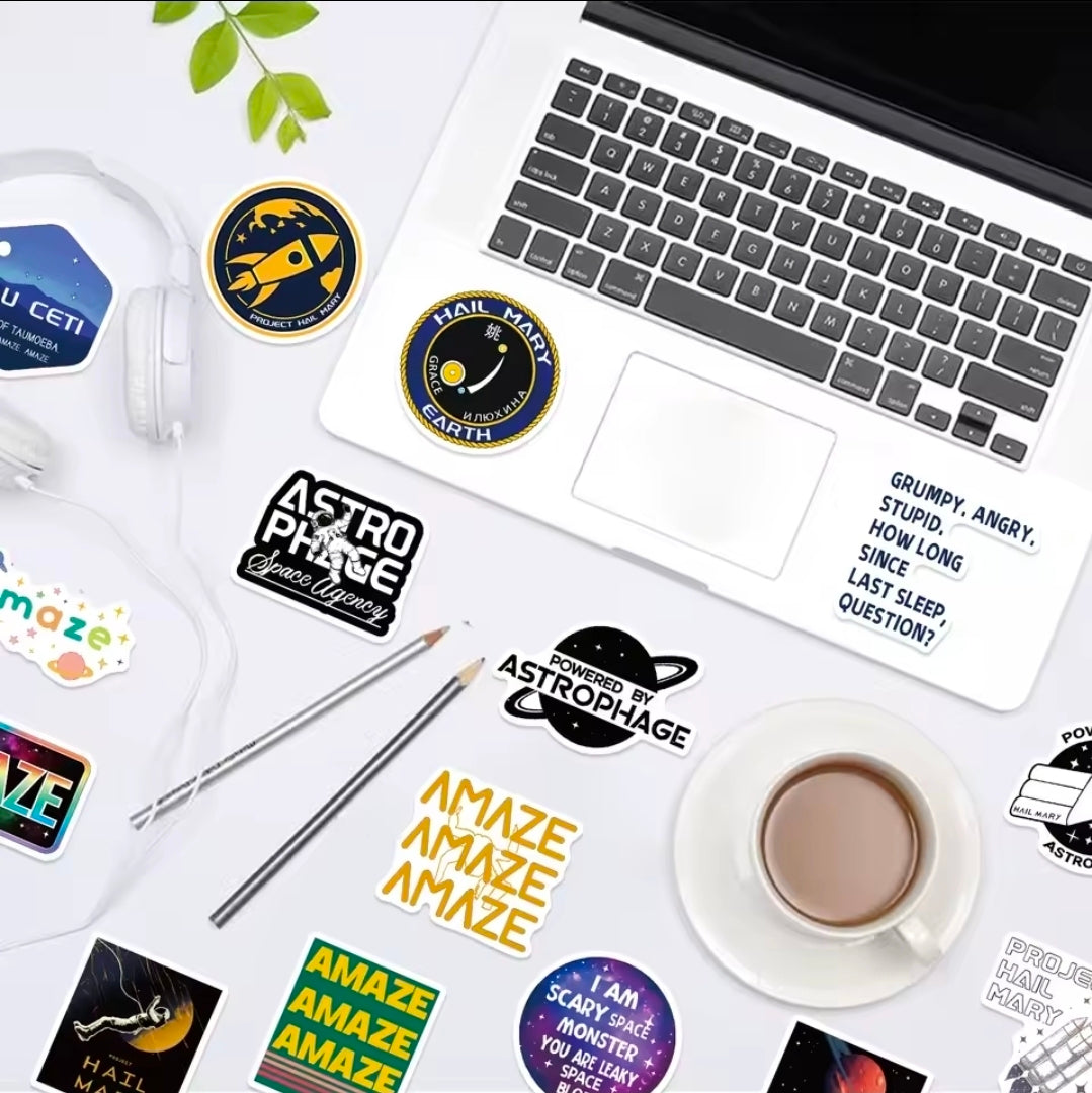 Space-themed vinyl stickers on laptop and desk: round logos, warning badge, and text icons