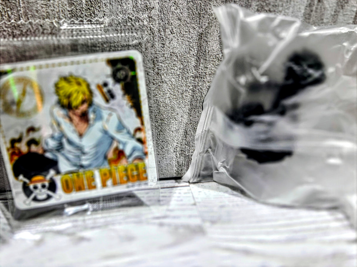 Sealed bag with small black collectible figure and One Piece character card (yellow figure)