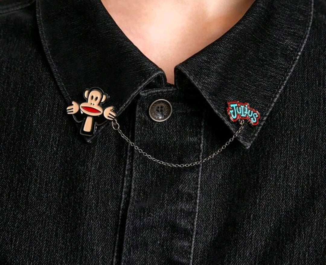 Enamel pin set on dark denim jacket: Julius monkey face and Tutius logo pin