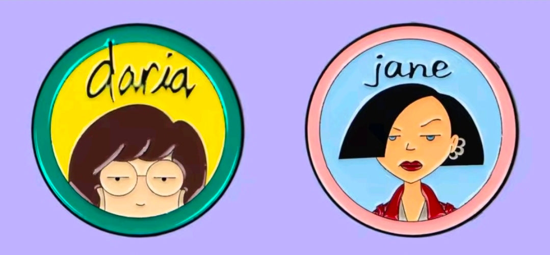 Two circle character enamel pins: Daria (green) and Jane (pink)