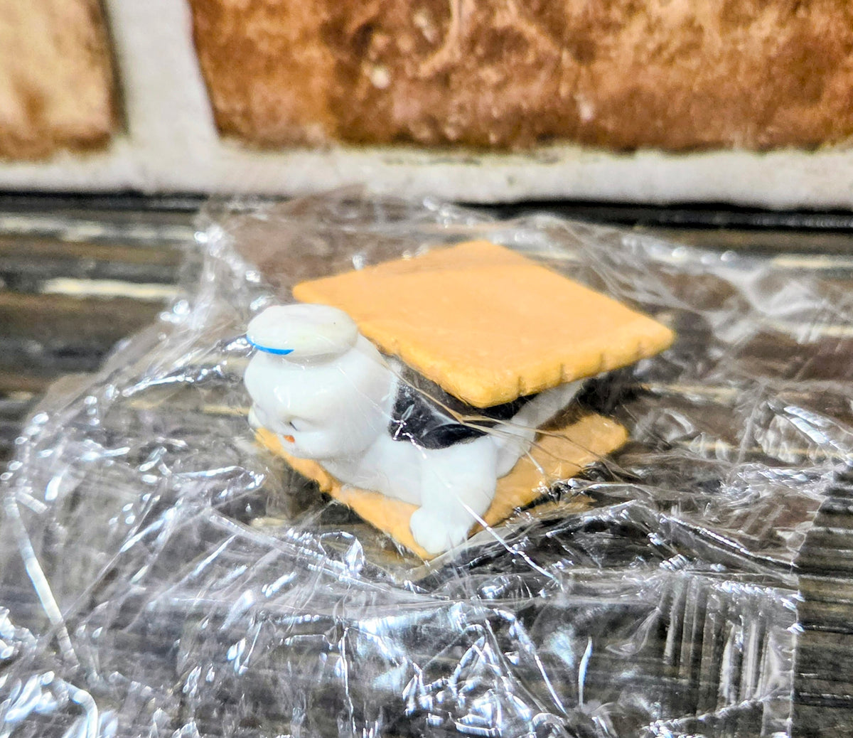Toy mini figure with graham cracker and dark chocolate piece, wrapped in clear plastic