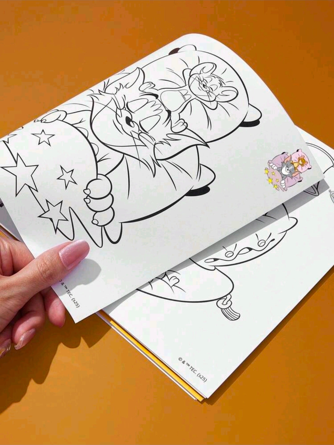 Spiral-bound coloring book with black-line cartoon scenes, open to two pages