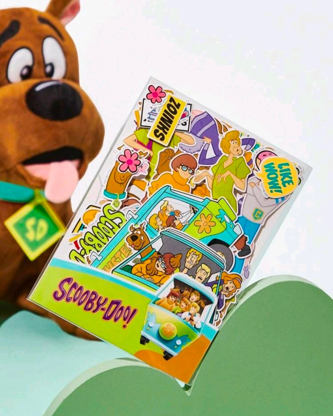 Scooby-style sticker sheet with character scenes and icons, held against a plush dog