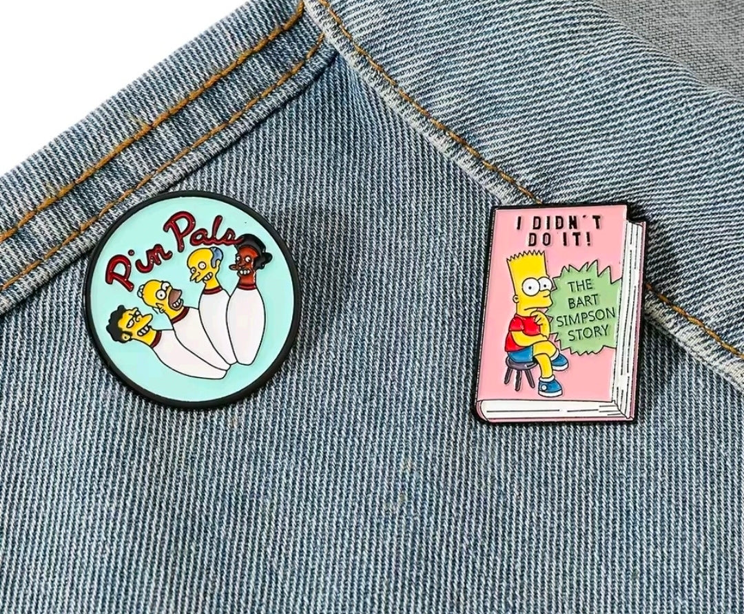 Simpsons enamel pin set on denim: round Pin Pals pin and pink book-shaped pin