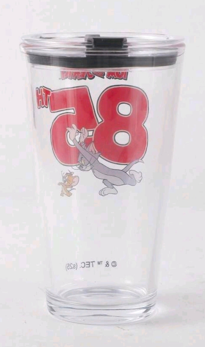 Clear glass tumbler with black lid, Tom & Jerry 85 logo and text