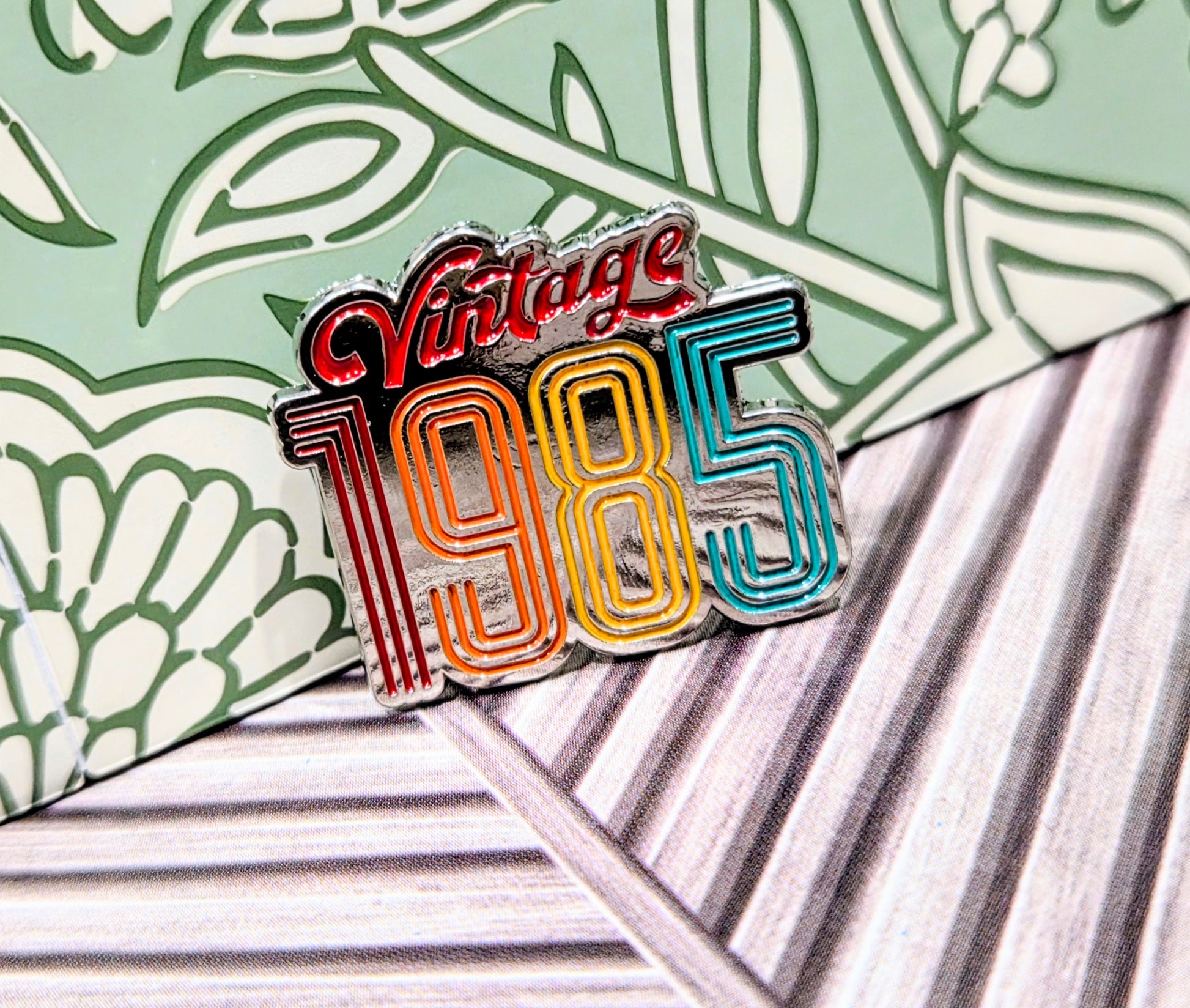 Enamel pin with 'Vintage 1985' rainbow striped lettering