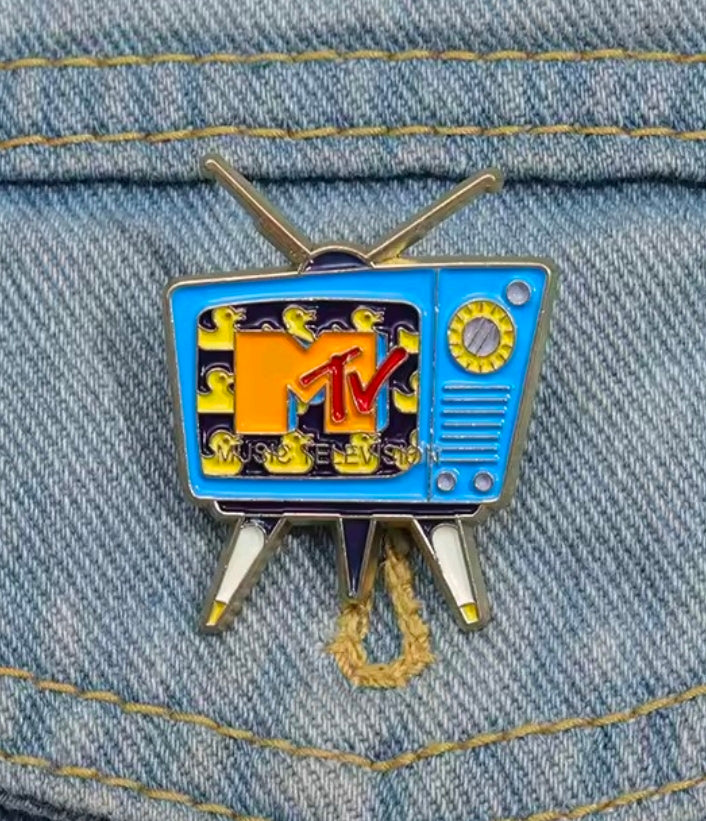 Retro TV enamel pin attached to denim fabric, blue screen with MTV logo and gold antenna