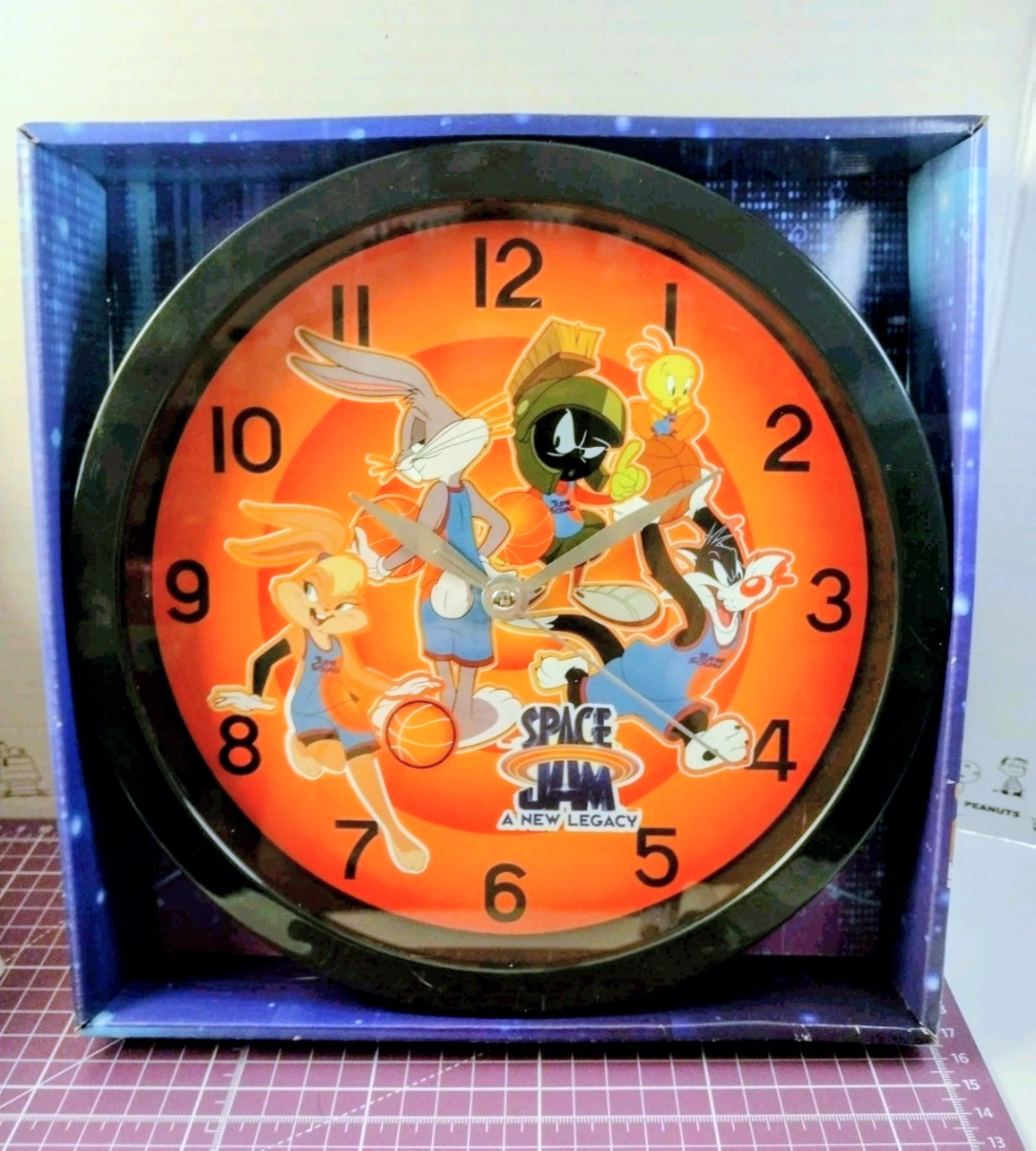 Analog wall clock with orange dial, black rim, and Space Jam character illustration