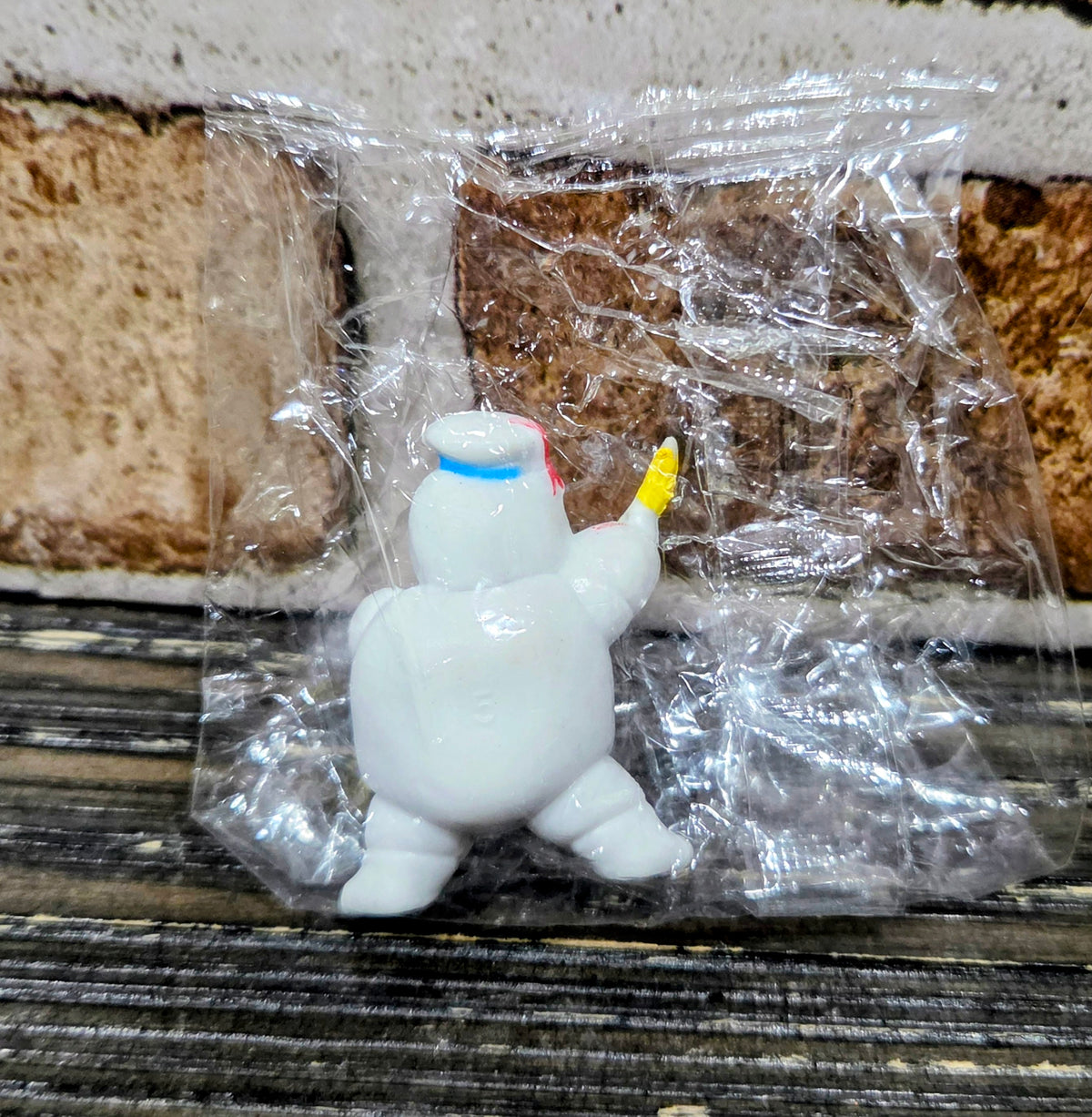 White mini figure crouching, blue bib, holding yellow wand, sealed in clear plastic