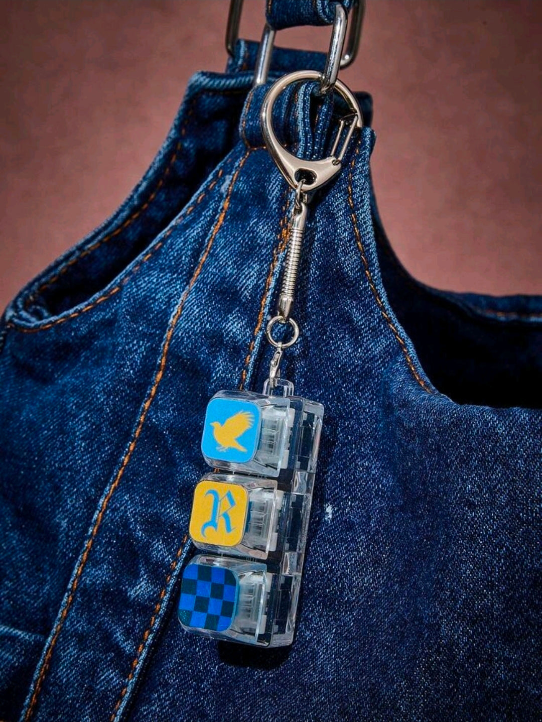 Ravenclaw keychain charm attached to denim bag, silver rings and clear blocks with bird and checkers