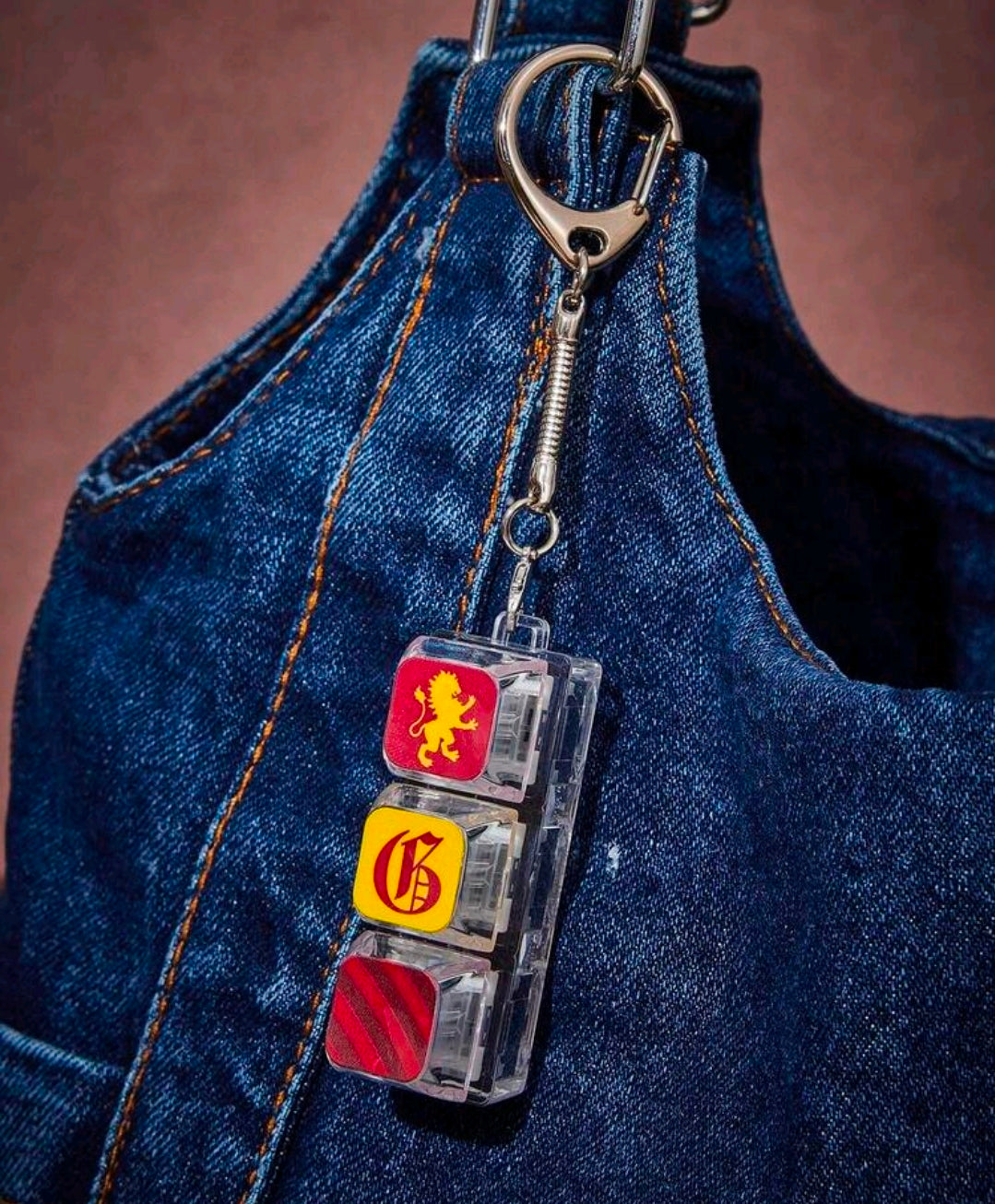Keycap fidget keychain charm hanging from blue denim bag, lion, crest, and red stripes