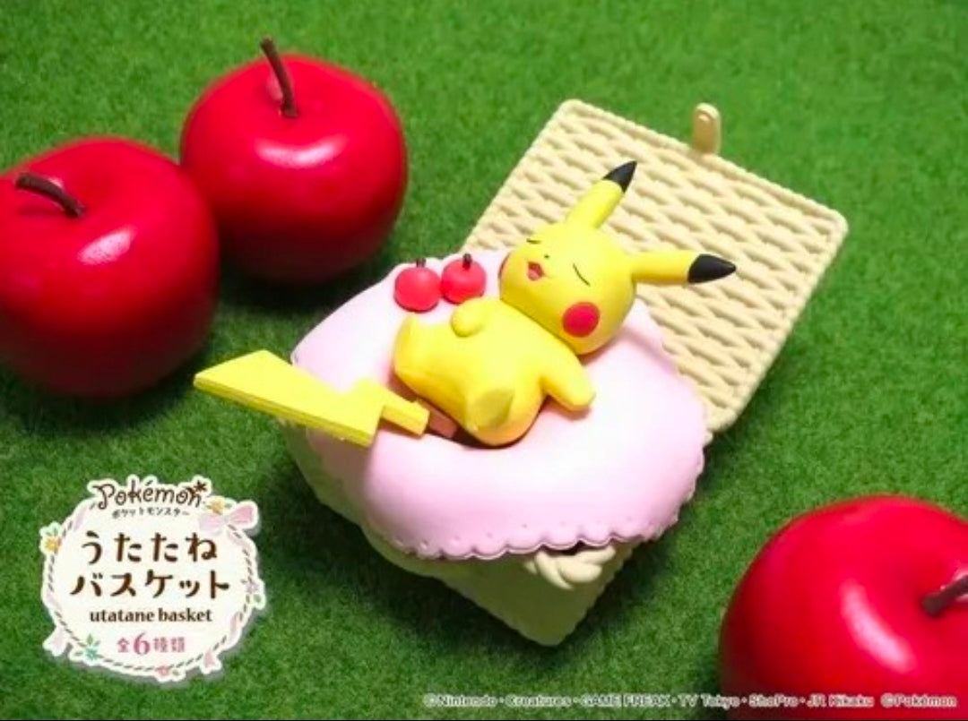 Miniature Pikachu on a pink cushion inside a woven basket with red apples on grass