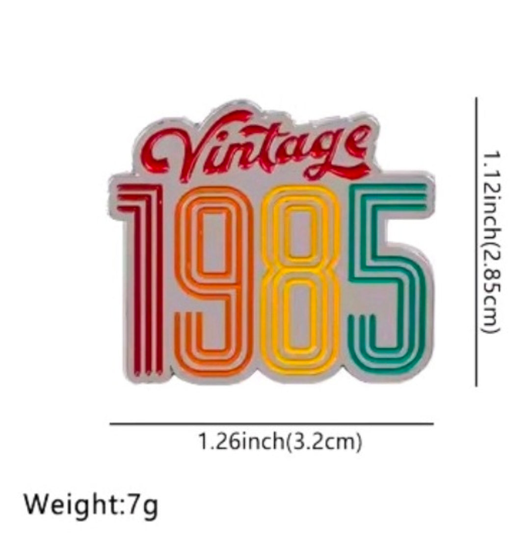 Enamel pin with 'Vintage 1985' rainbow striped text on white card