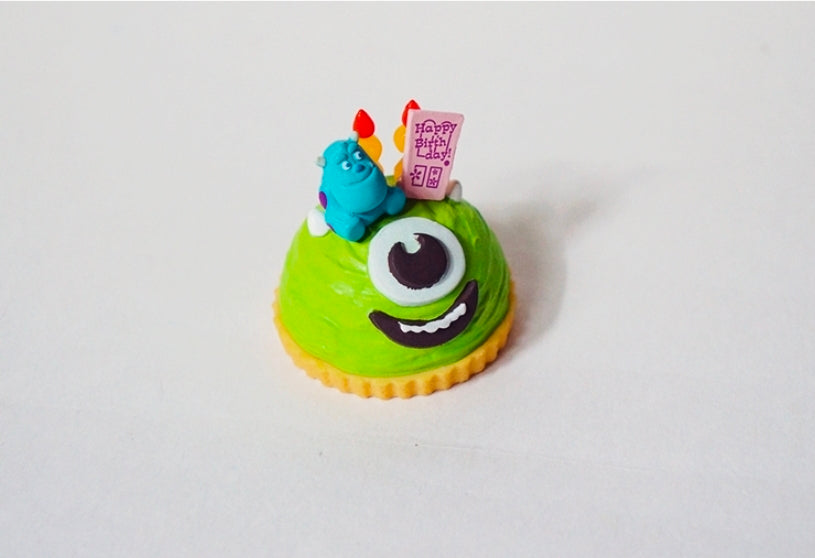 Green sponge cake mini figure with teal Sulley on top and Happy Birthday card
