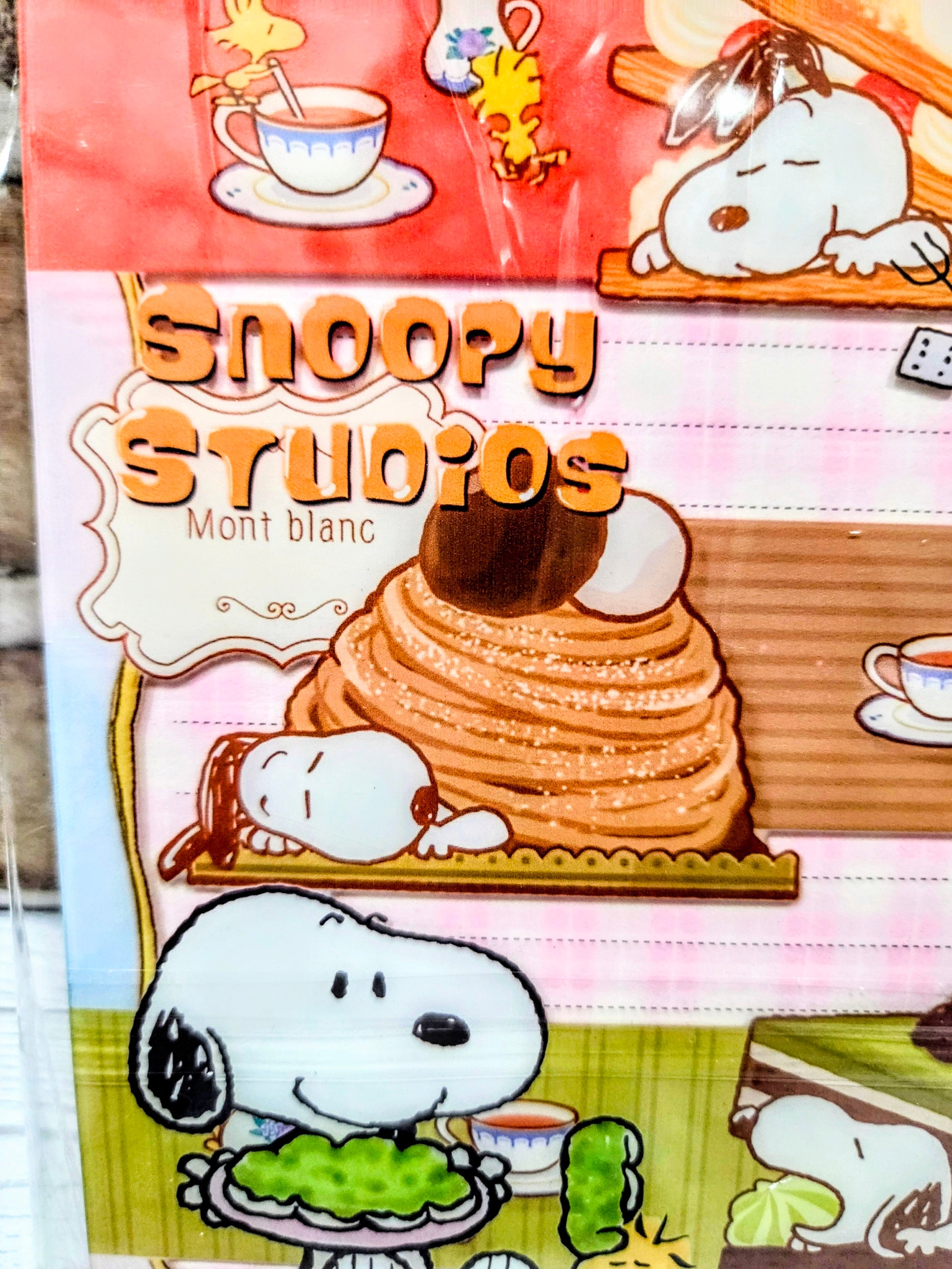 Close-up A5 acrylic shaker notebook showing Snoopy Studio title and dessert food artwork.