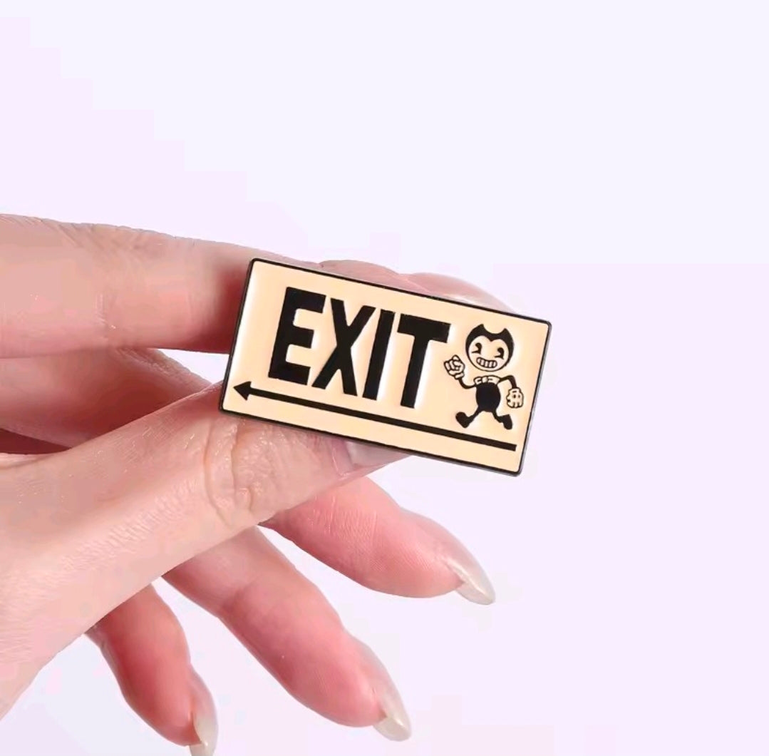 Enamel pin with an EXIT sign and small hooded character, held between fingertips