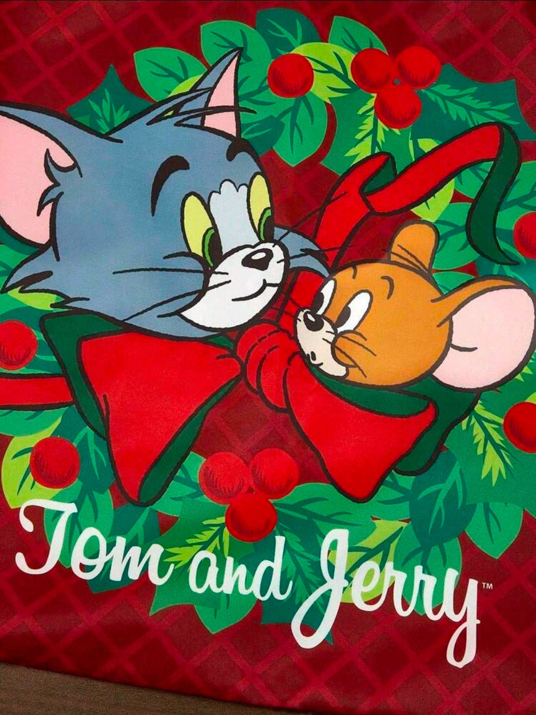 Red and green holiday tote bag with Tom and Jerry character print and logo.