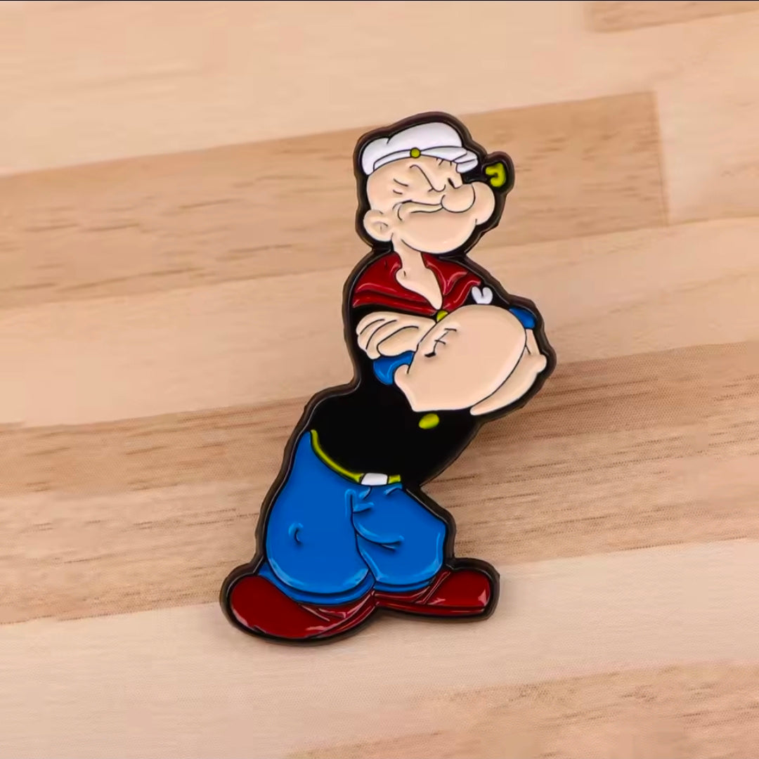 Cartoon sailor enamel lapel pin, seated pose with red shirt and blue pants.