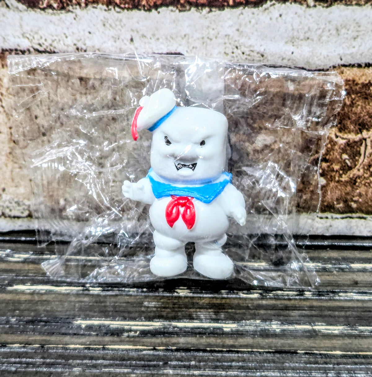 White mini figure in clear wrap, red hat and blue bib, red chest emblem