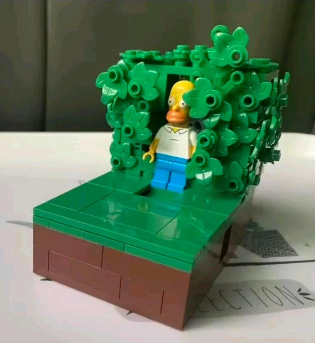 Brick playset with dark green foliage, brown platform base, and Homer-style minifigure figure.