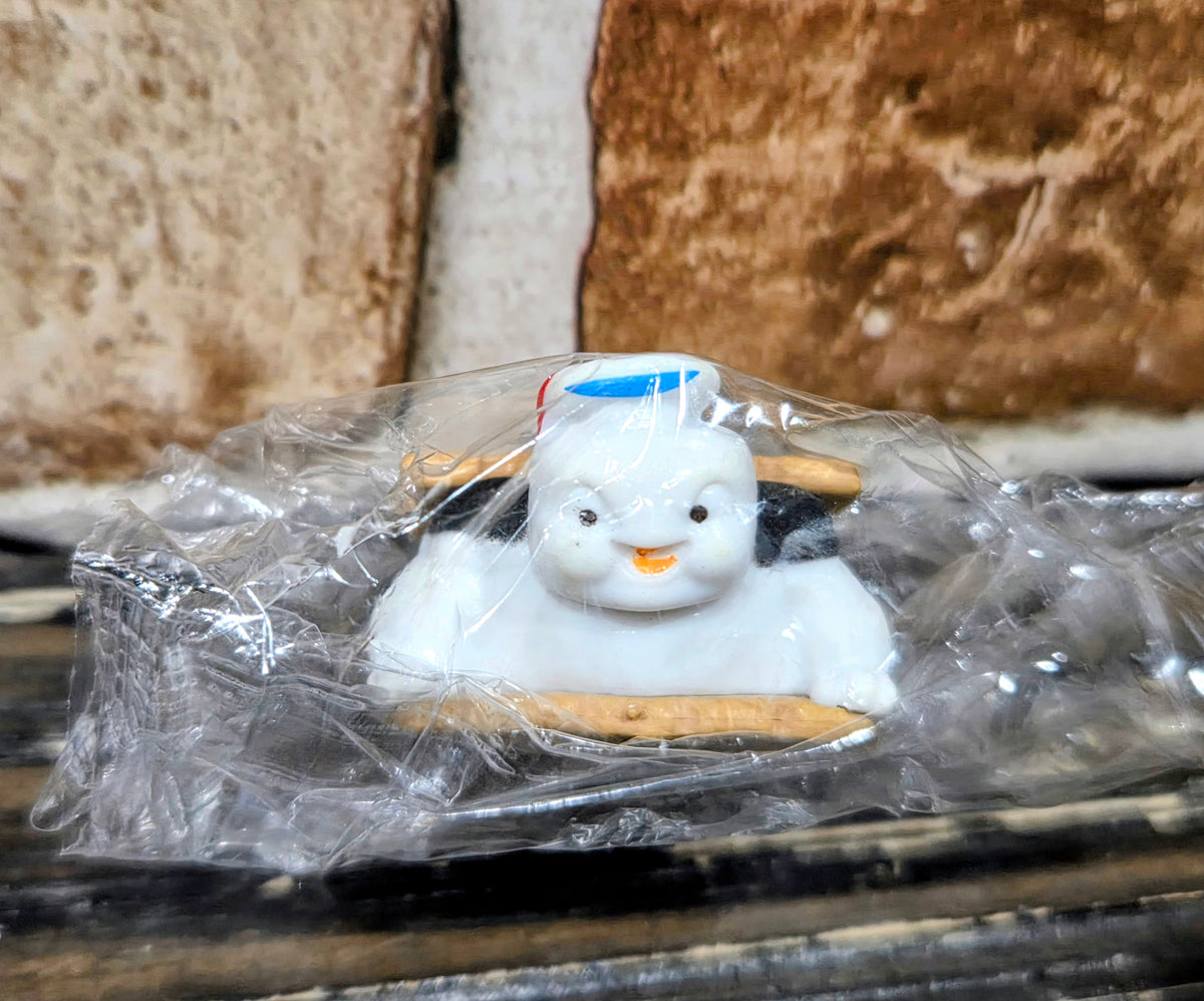 Toy mini figure with white body on graham cracker base, sealed in clear plastic