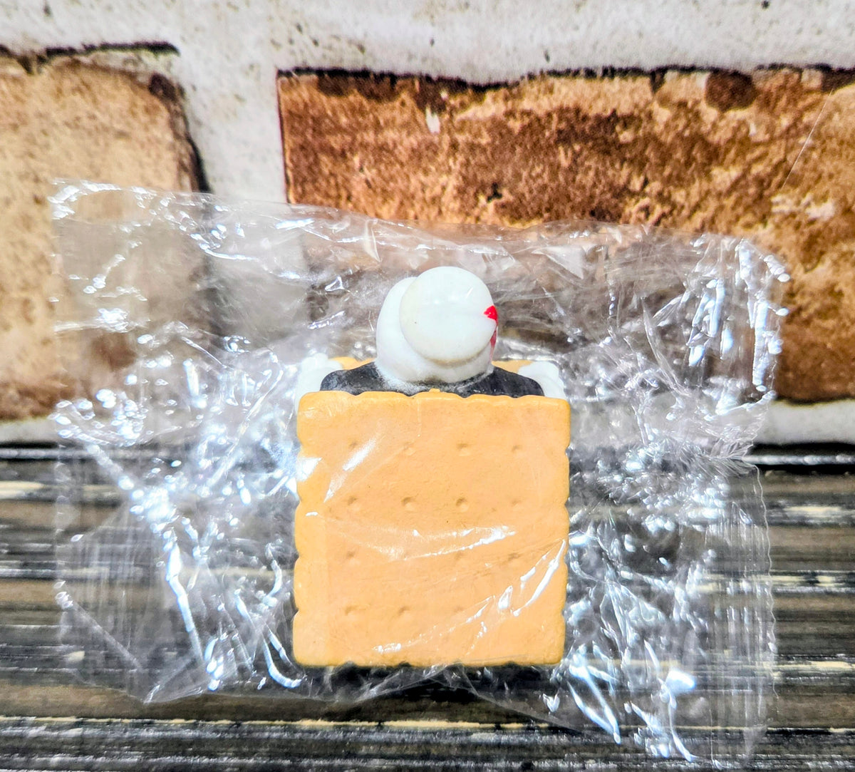Toy s'mores mini figure with graham cracker square and white marshmallow, sealed in plastic