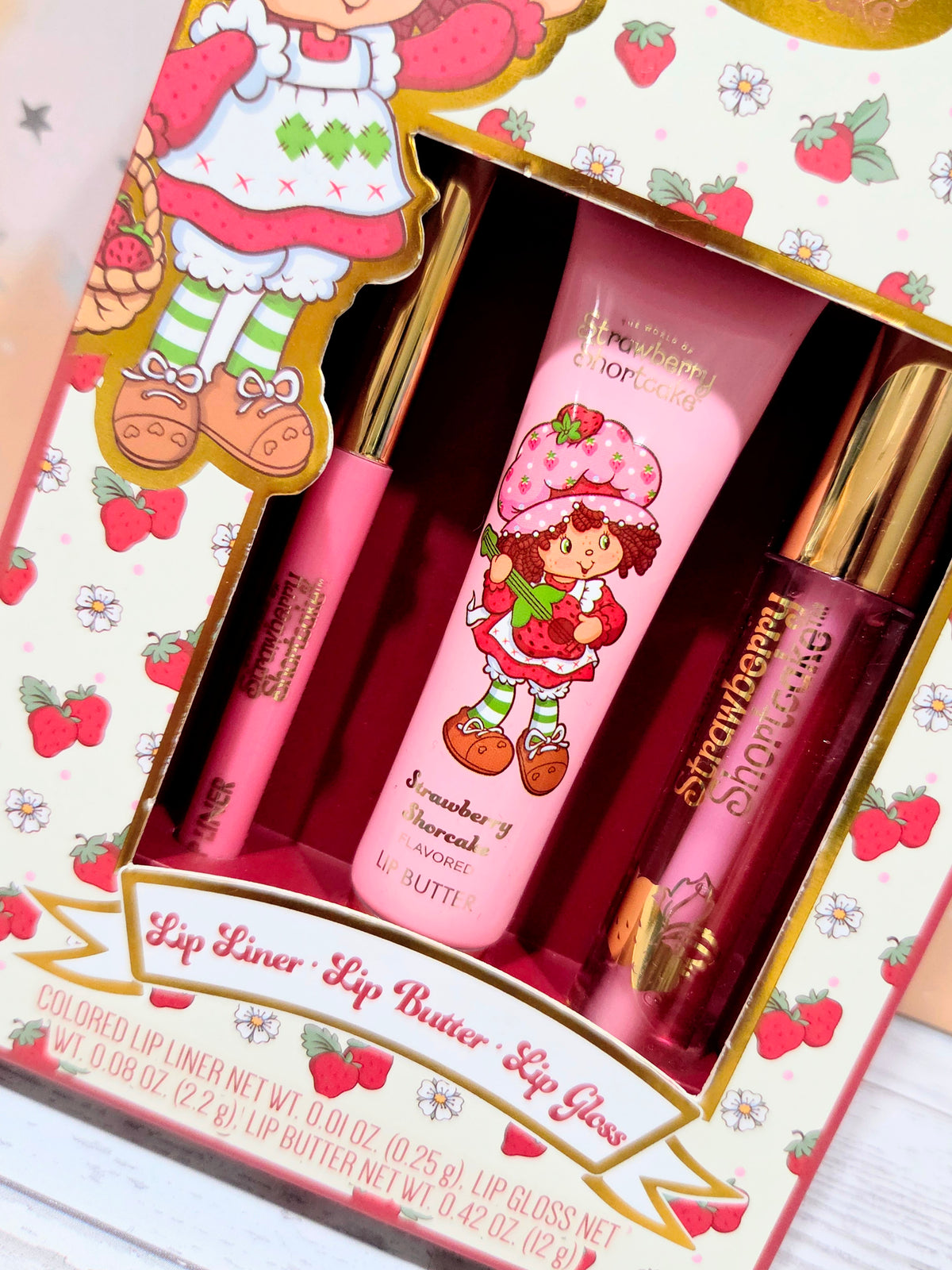 Open lip kit with pink lip butter bottle and gold-toned lip gloss and liner