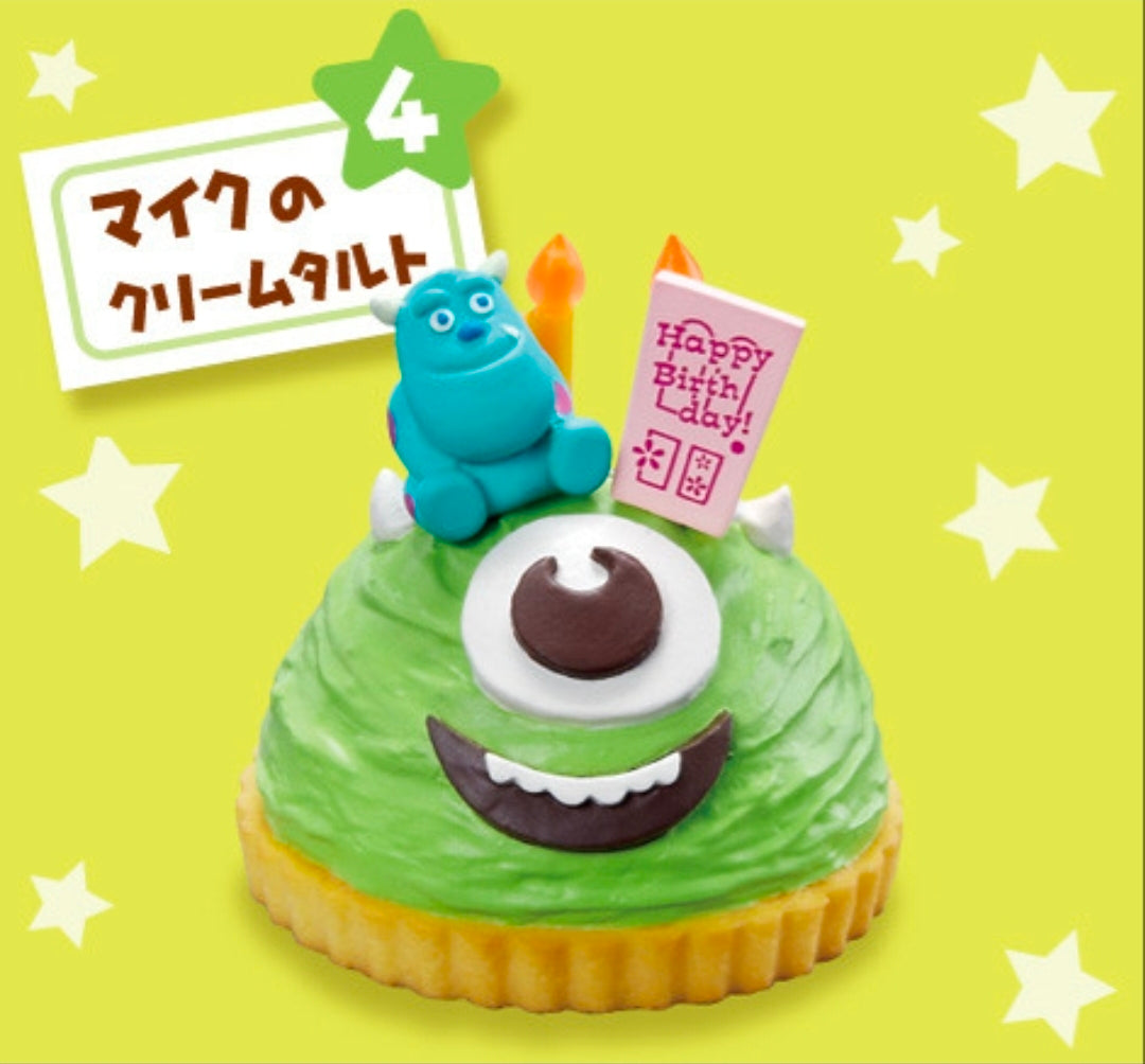 Green sponge cake mini figure with teal monster holding Happy Birthday card and orange candles