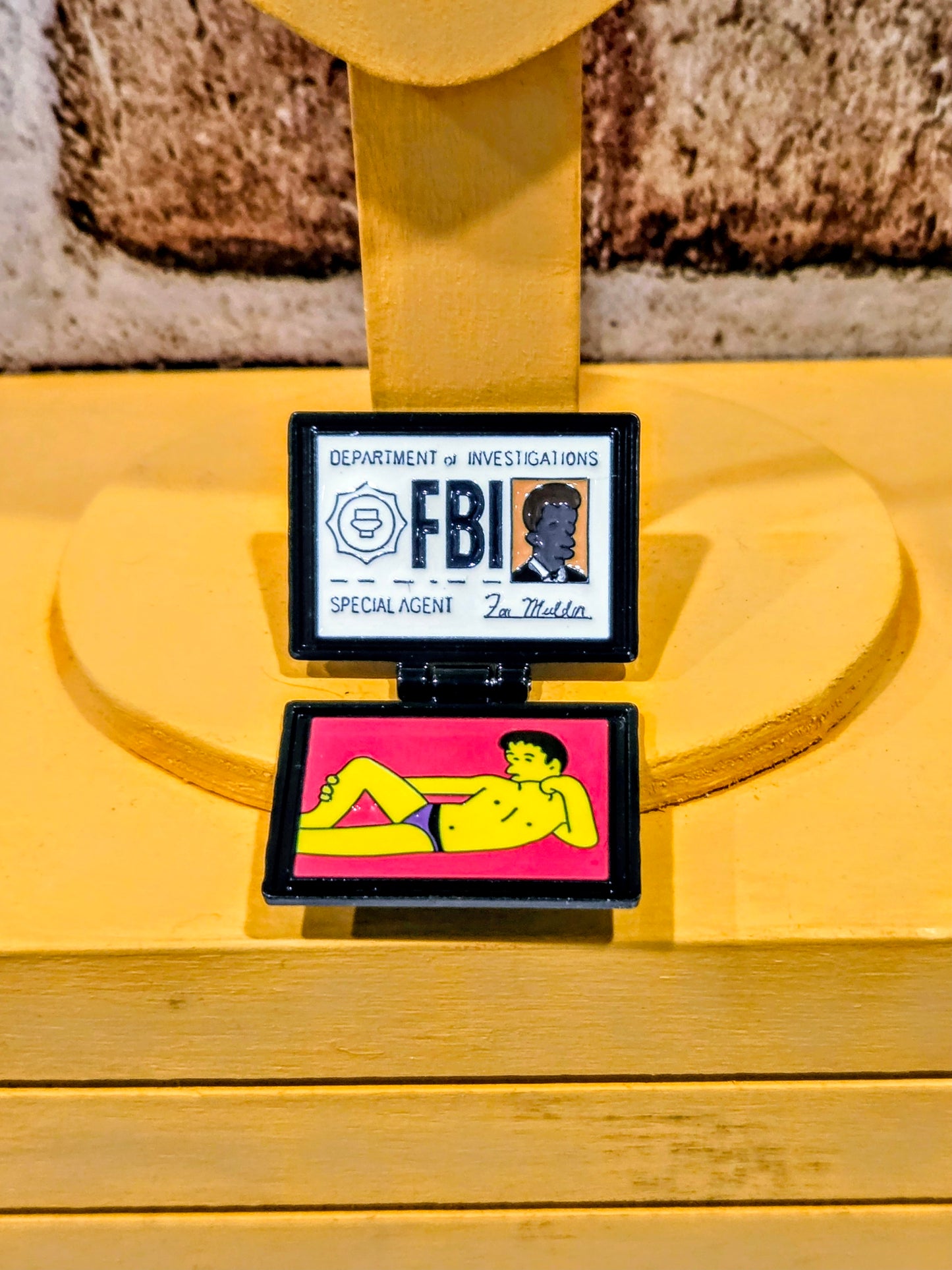 Enamel pin with open front panels: “FBI” badge on top and character artwork below.