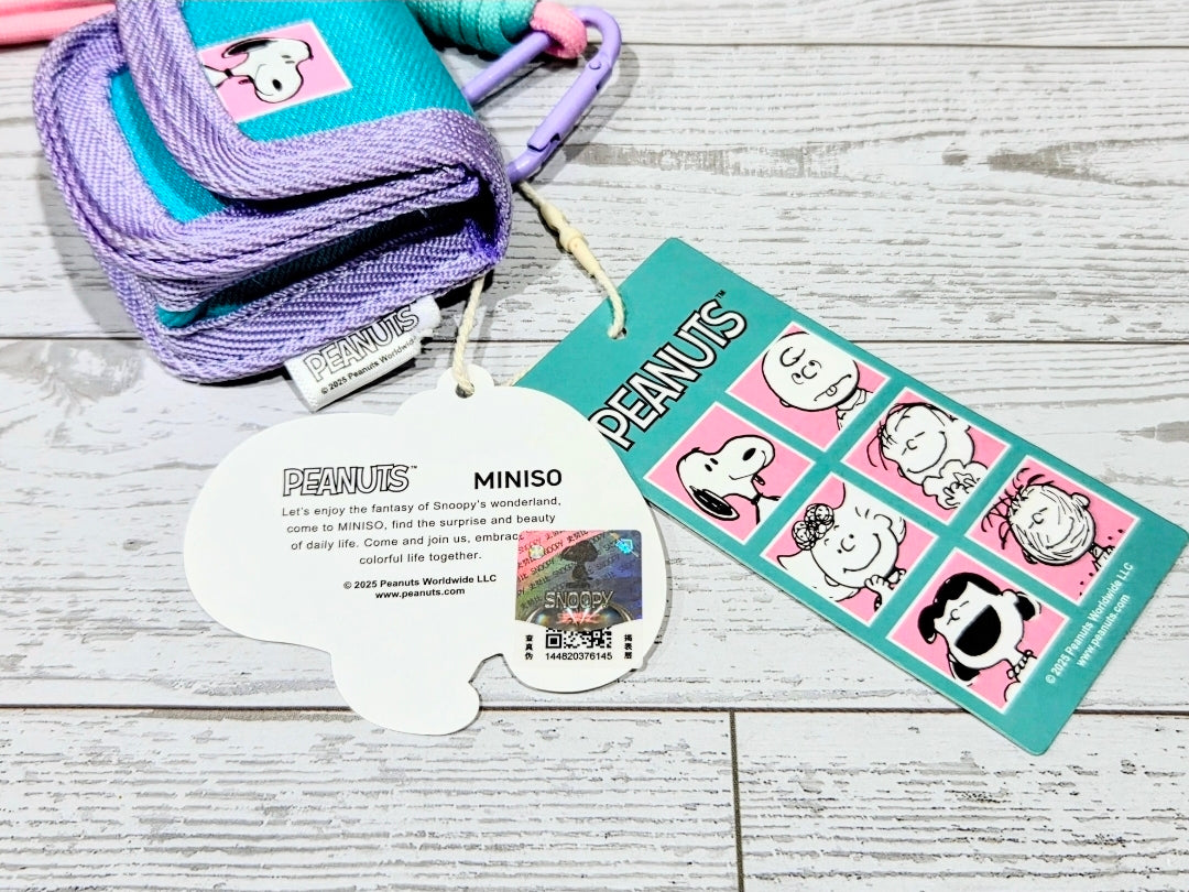 Close-up of teal and purple canvas earbud case with Snoopy patch and product card