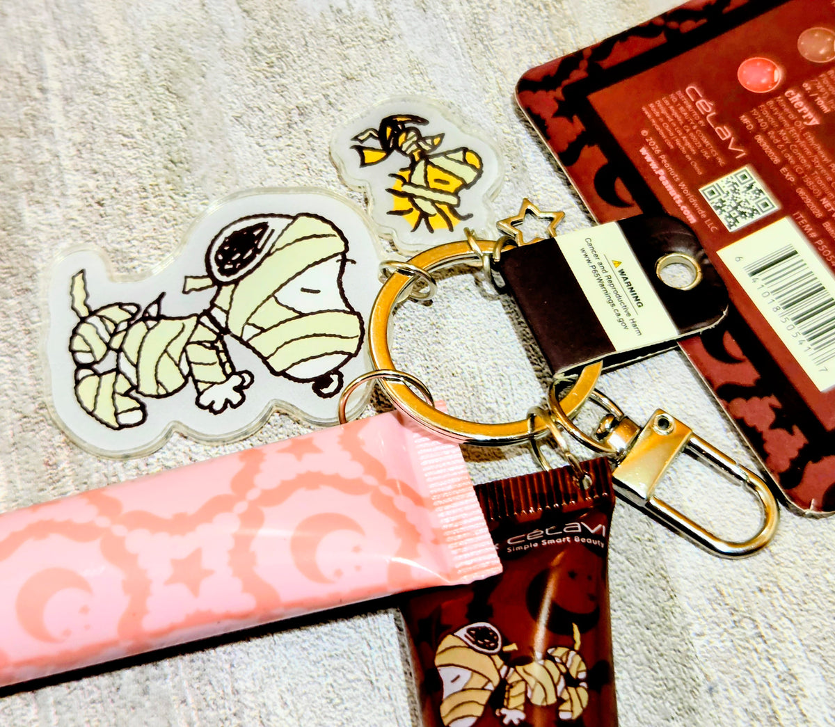 Peanuts-themed keychain with two sticker charms beside lip gloss tubes