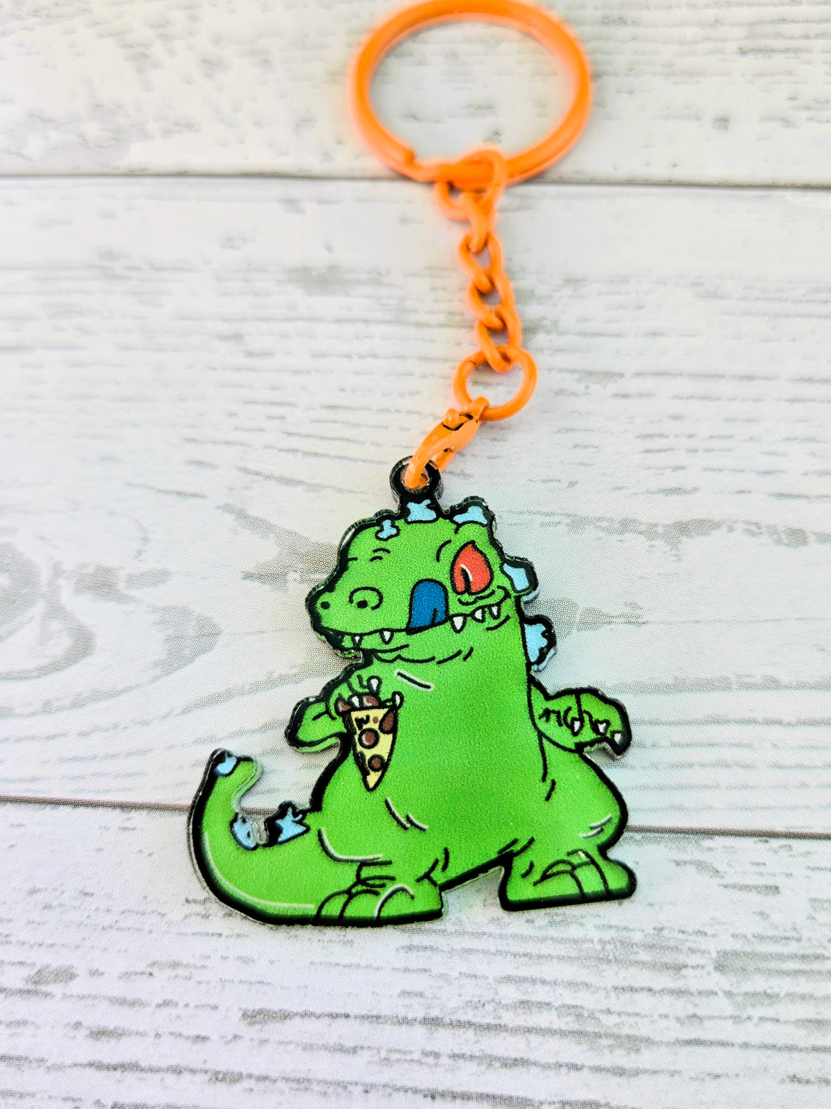 Orange-ring acrylic keychain with green Reptar crouching, red mouth detail, orange chain