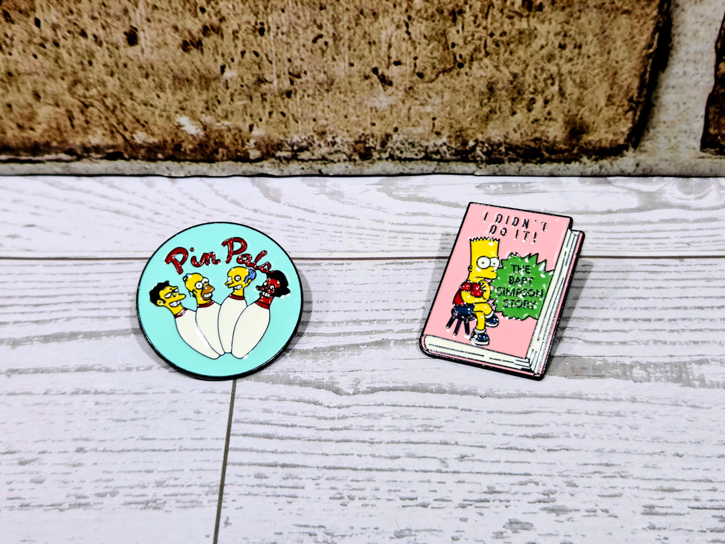 Simpsons enamel pin set: round turquoise Pin Pals pin and pink book-shaped pin