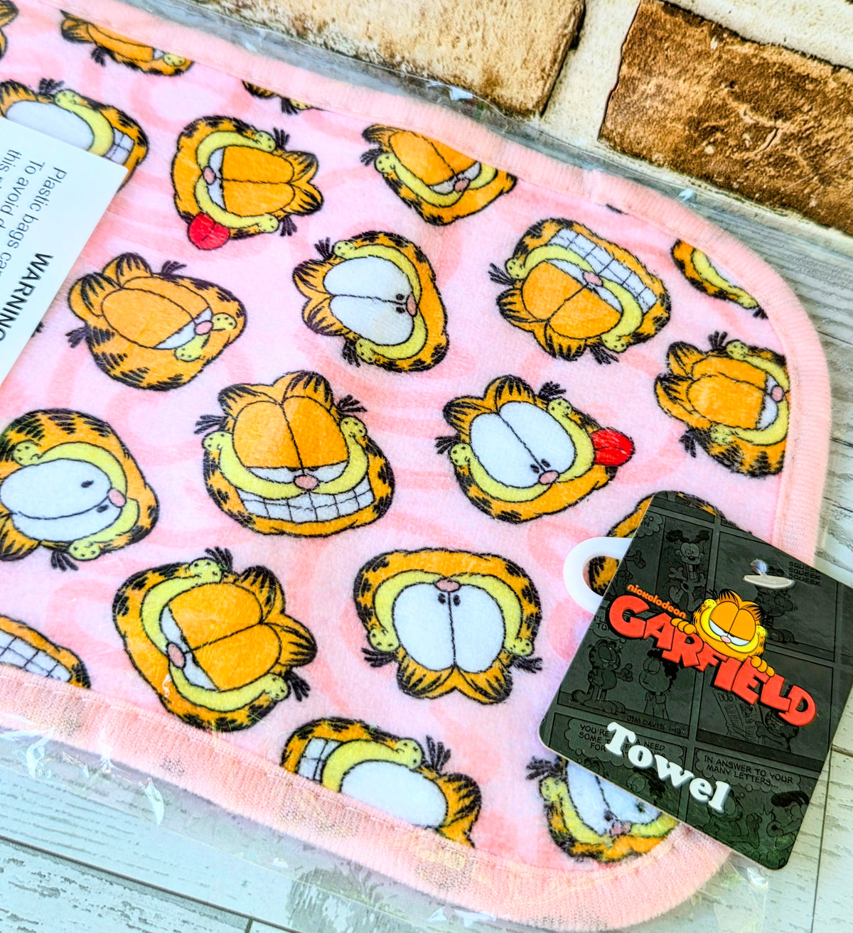 Pink cloth with repeated Garfield-style cat faces in yellow and white, scalloped trim.