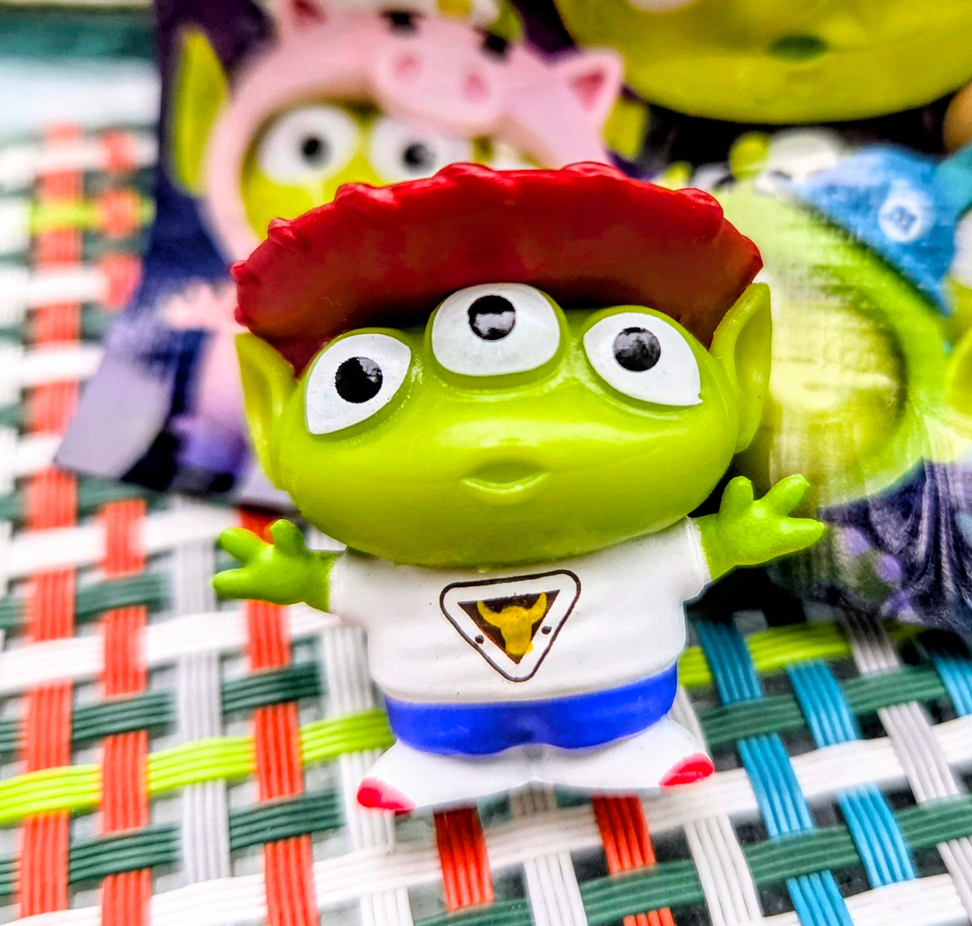 Close-up green alien mini figure with red pizza-slice hat, white shirt with triangle emblem