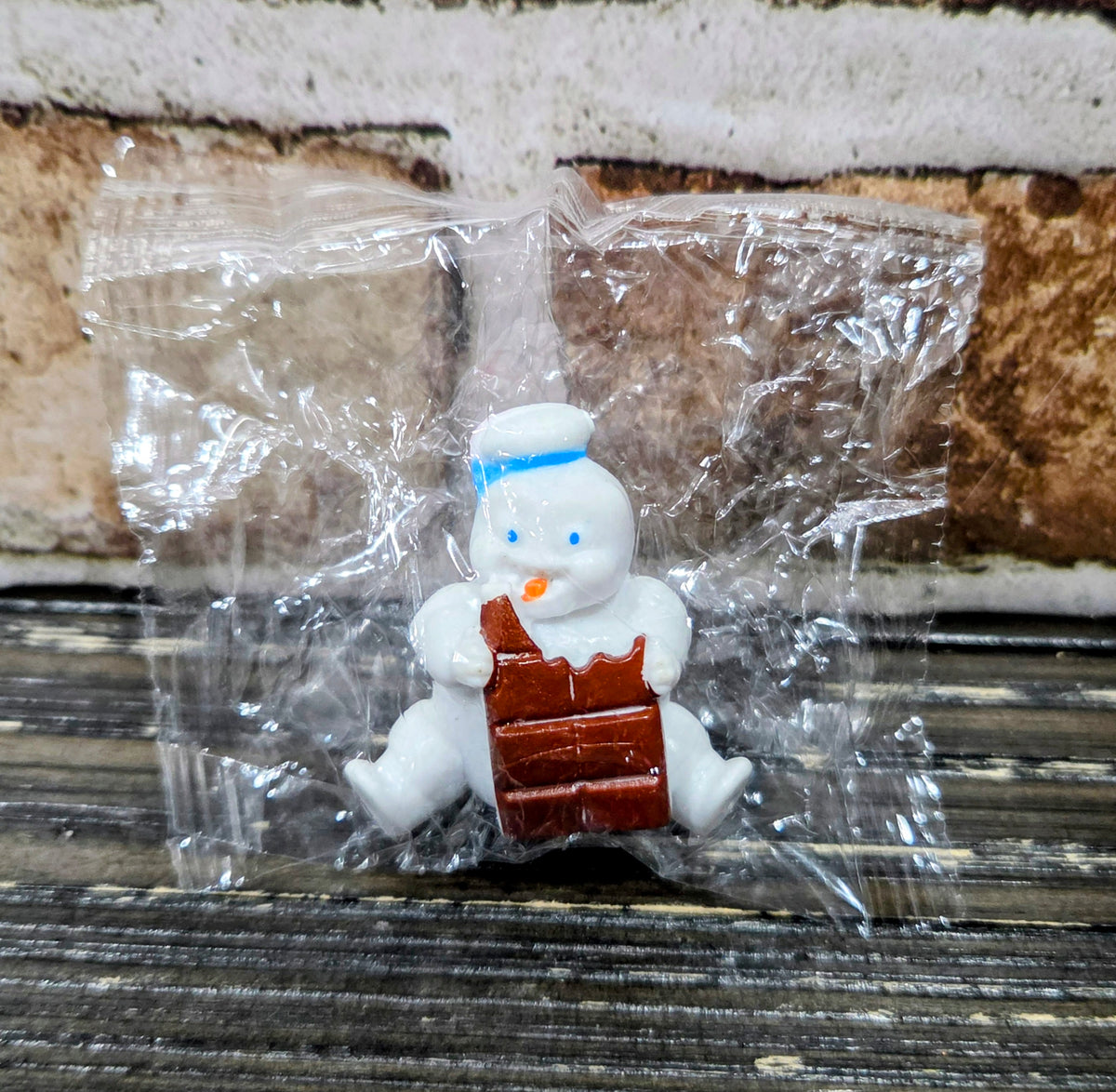 White mini Puft figure seated with a brown chocolate bar, striped hat on head.