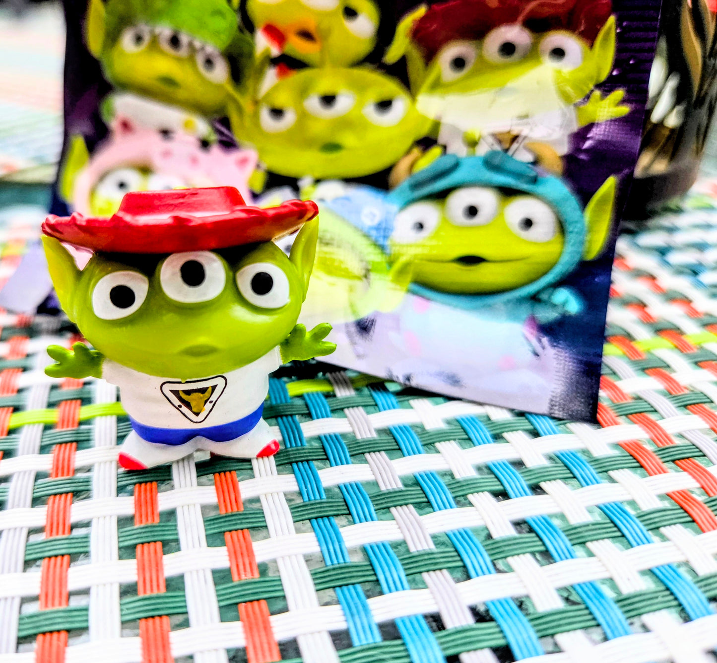 Multiple alien mini figures with large eyes and colorful hats on a woven mat