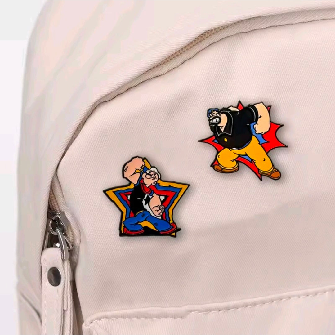 Two cartoon enamel lapel pins on light fabric: Brutus and Popeye.