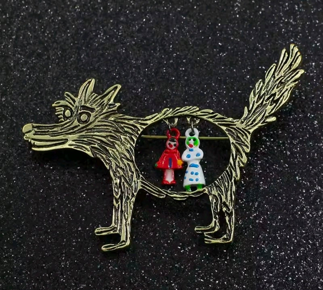 Gold-tone enamel wolf brooch pin with circular Red Riding Hood and grandma charms on dark background.