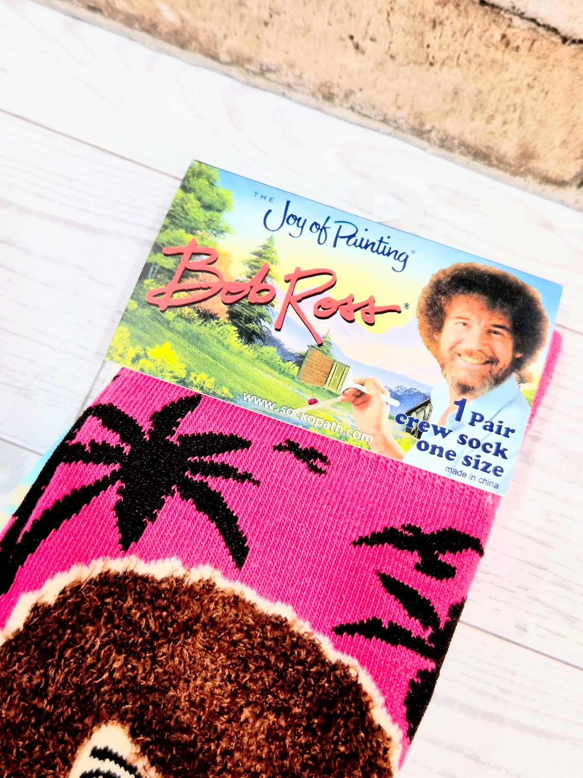 Pink crew sock with Bob Ross style face graphic and colorful text elements