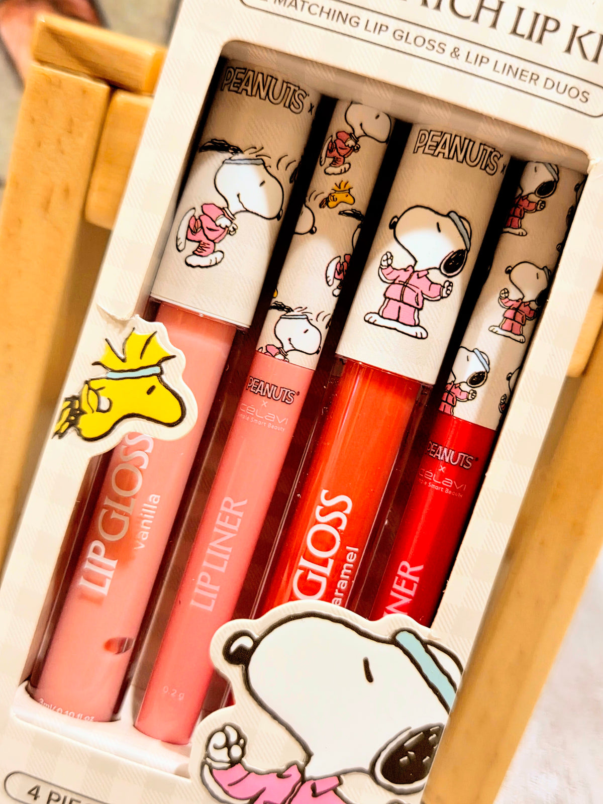 Lip gloss and lip liner duo tubes arranged in a box with Peanuts character art.