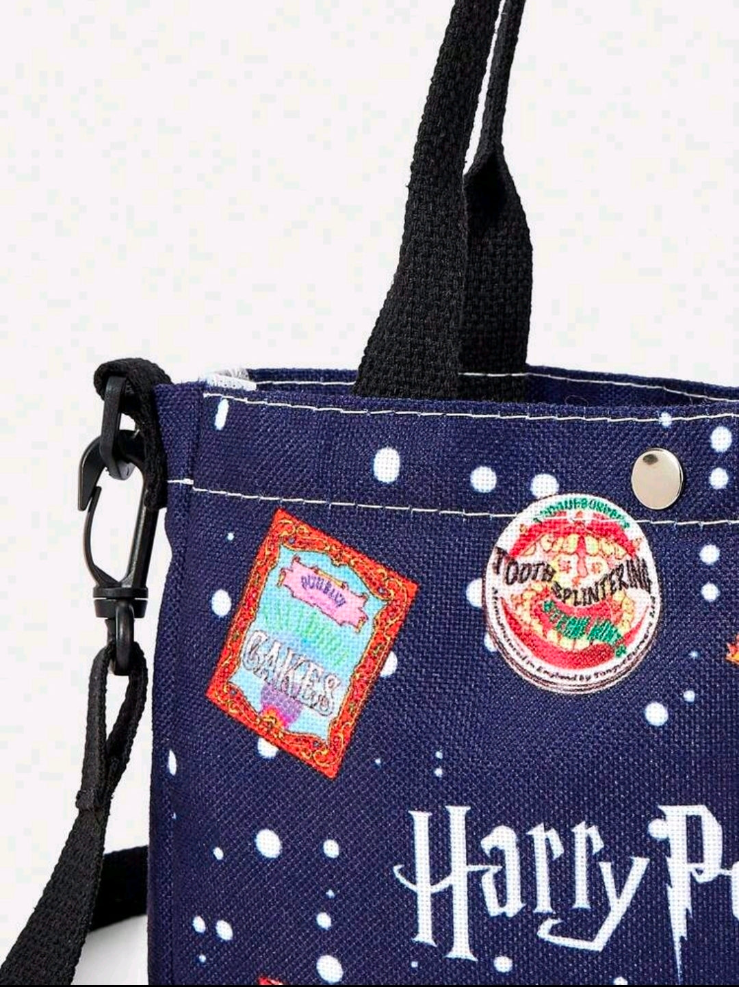Navy canvas tote bag with colorful front patches, black crossbody strap, white polka dots